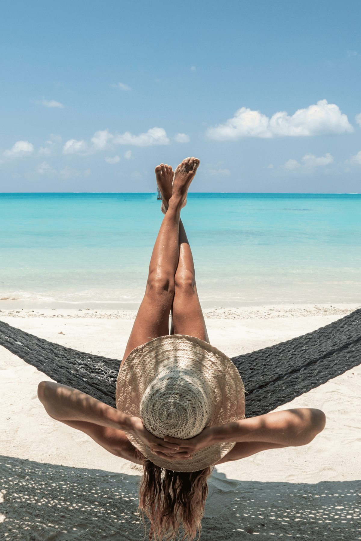 luxury travel showing a woman with a hat relaxing on a beach with clear water