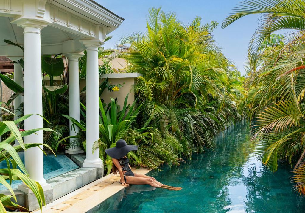 luxury hotel pool with palm trees and an elegant lady wearing a black hat